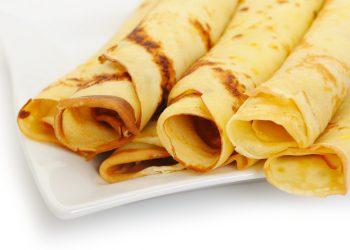 Crepe roll up a tubule on a plate. It is isolated on a white background.